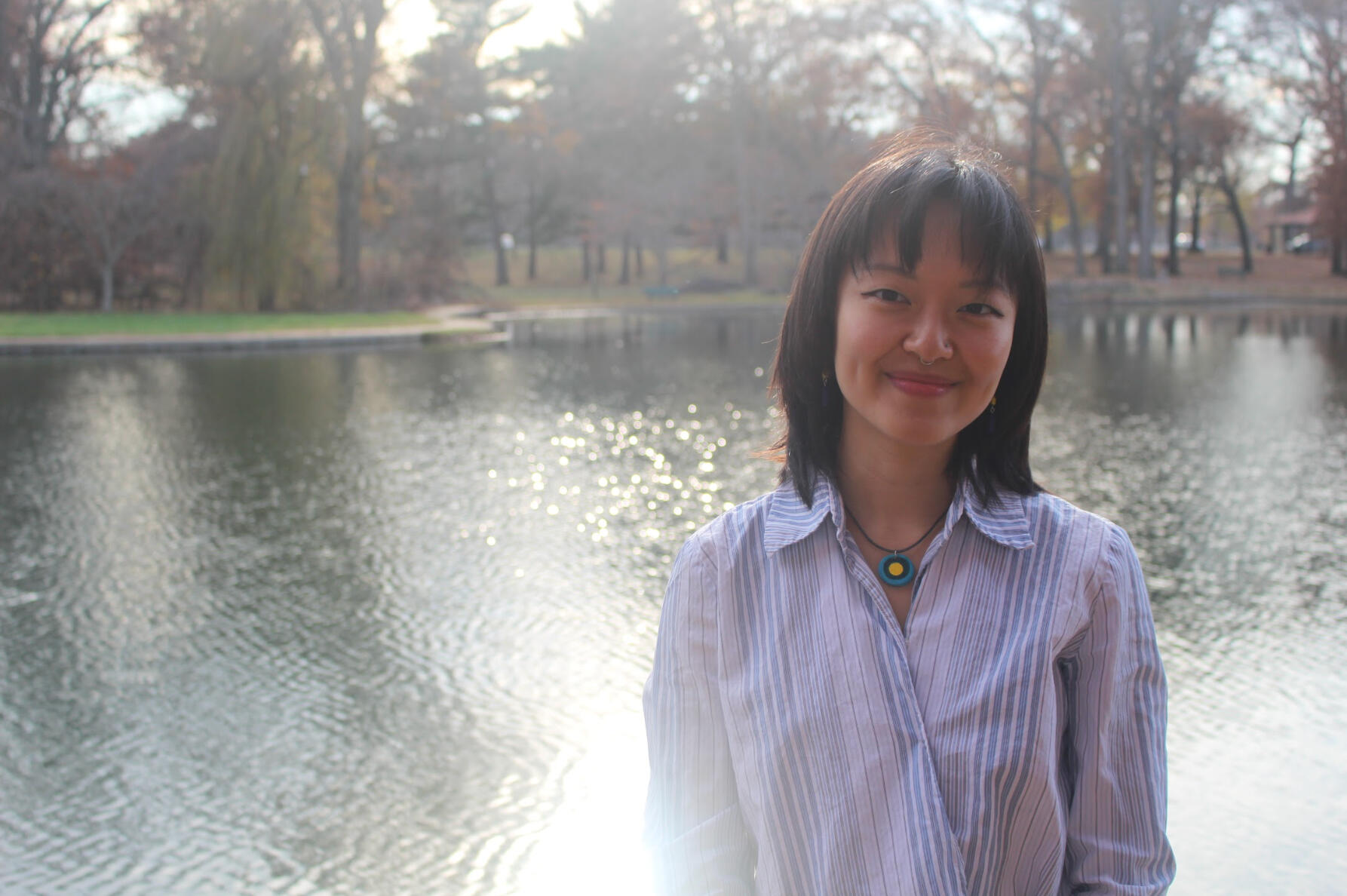 picture of an asian person in their 20's with shoulder-length black hair wearing a suit in greenery